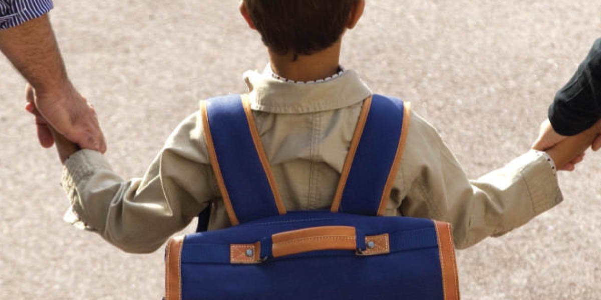 Un enfant portant un cartable, accompagné de deux adultes et photographié de dos.